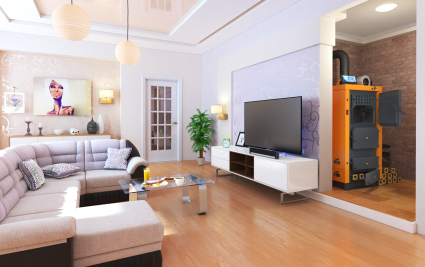 Living room with furnace, wood floors, couch, television, pendant lights, door, indoor plant, and TV stand