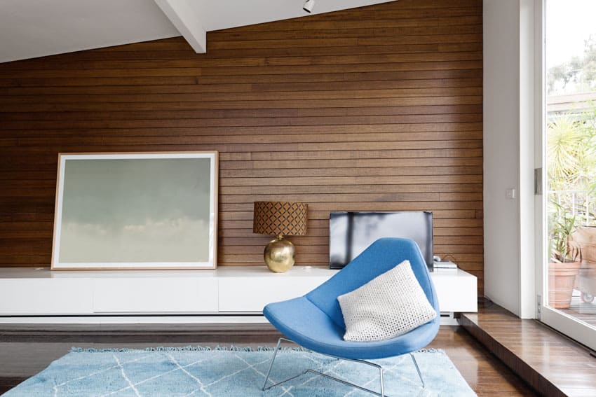 Room with horizontal beardboard panel wall. blue triangle chair and white floating table