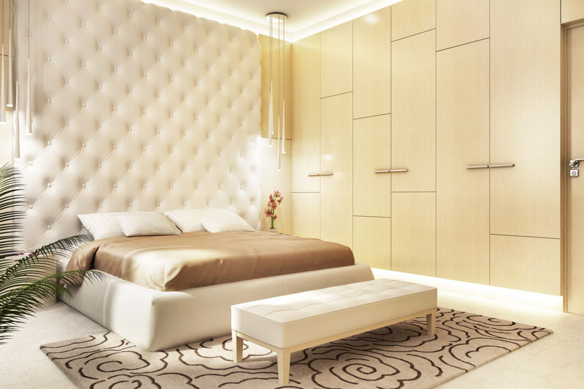 Luxury bedroom with rectangular ottoman bench, rug, bedding, pillows, headboard, pendant lights, and accent wall