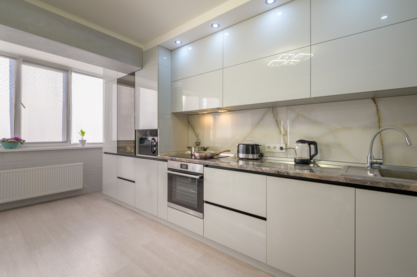 Minimalist kitchen with white cabinets, wood cabinets, oven, windows, and Calcatta gold backsplash