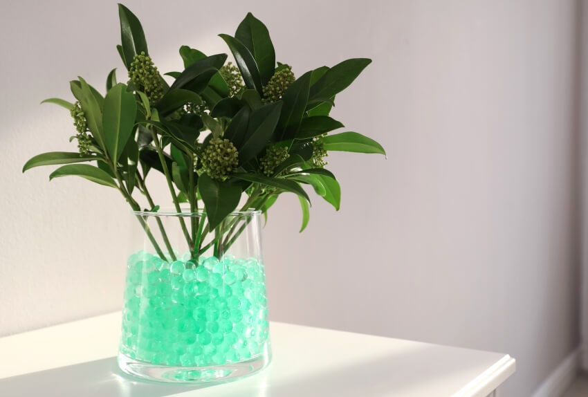 Mint green filler balls in glass vase with green plant on white table