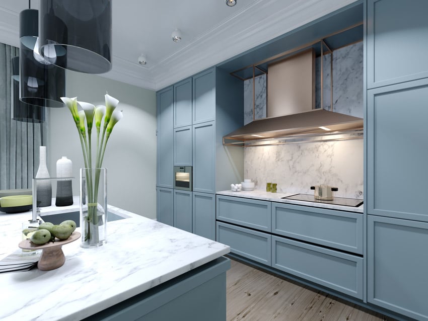 Modern kitchen with blue cabinets, marble slab backsplash, range hood, countertop, stove, and kitchenware