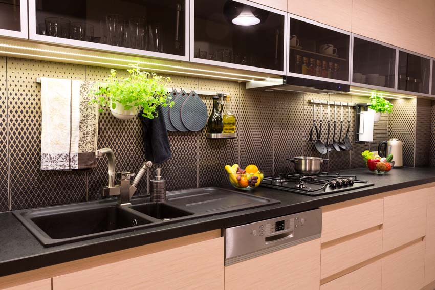 Modern kitchen with glass cabinets, diamond tile mosaic backsplash, black countertop, sink, faucet, and under cabinet lighting