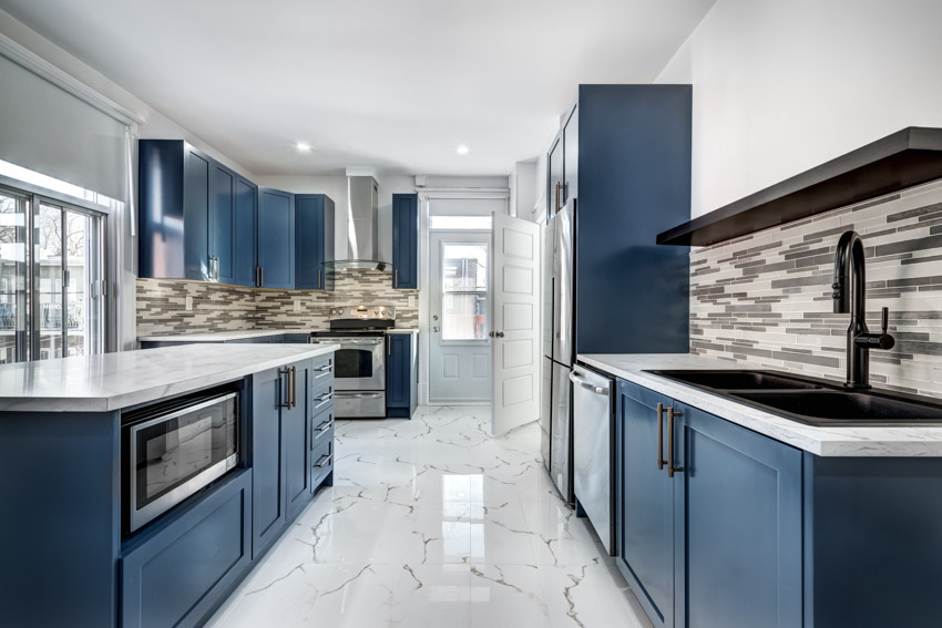 Modern kitchen with marble floors, blue cabinets, countertops, mosaic tile backsplash, sink, faucet, and windows