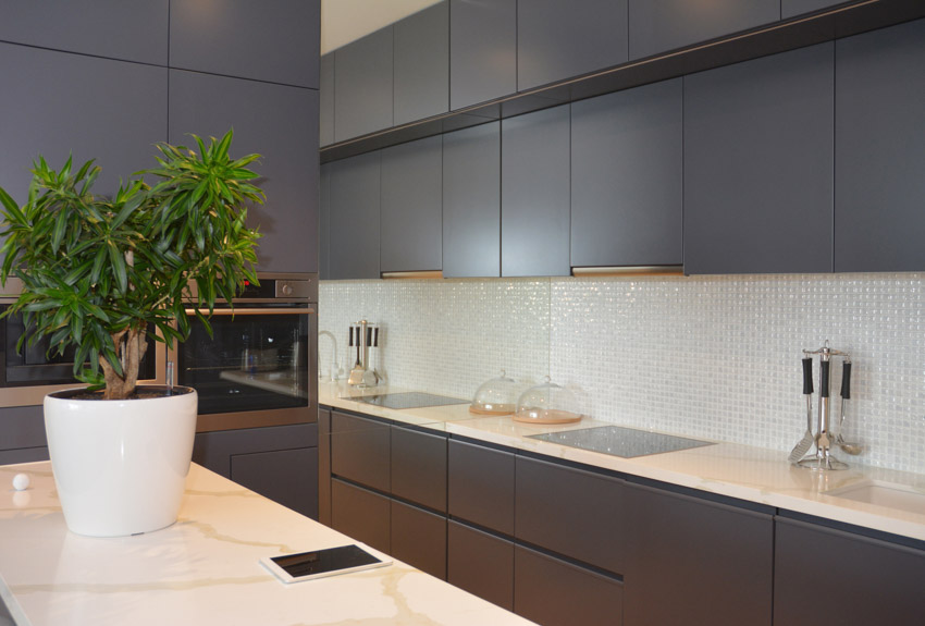 Modern kitchen with mosaic tile backsplash, marble countertop, stove, cabinets, and indoor plant