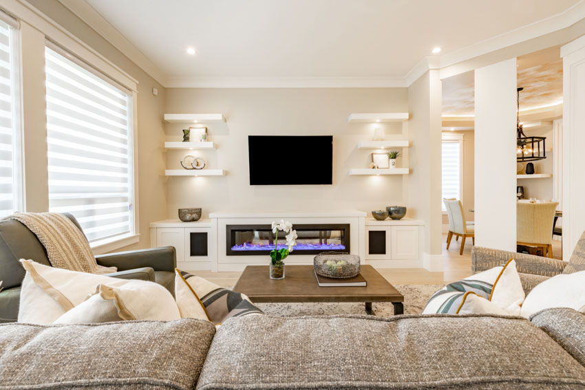 Room with floating shelves, above-fireplace television and windows with shades