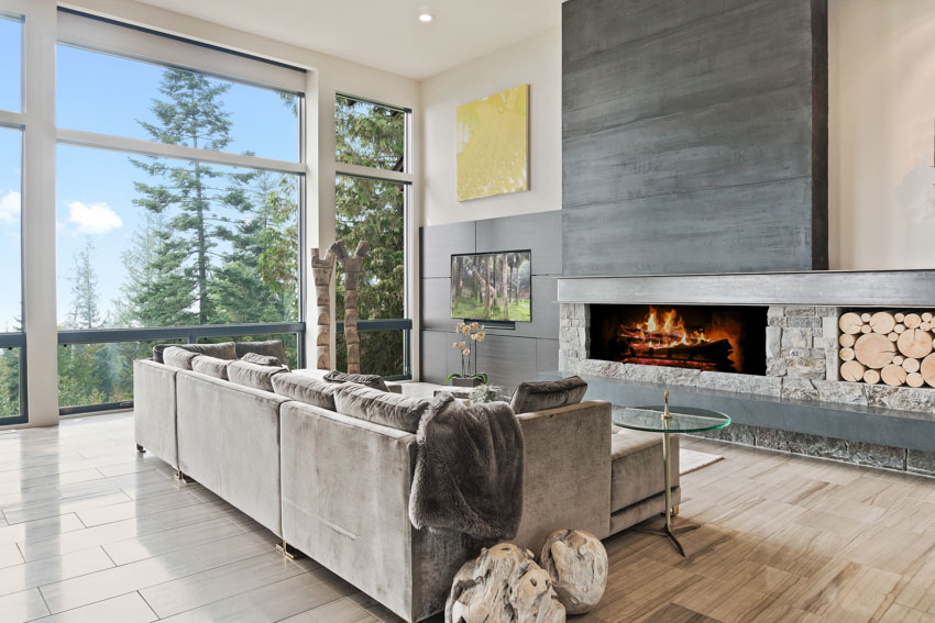 Modern living room with sofa, pillows, electric fireplace, concrete wall, wood flooring, and large windows