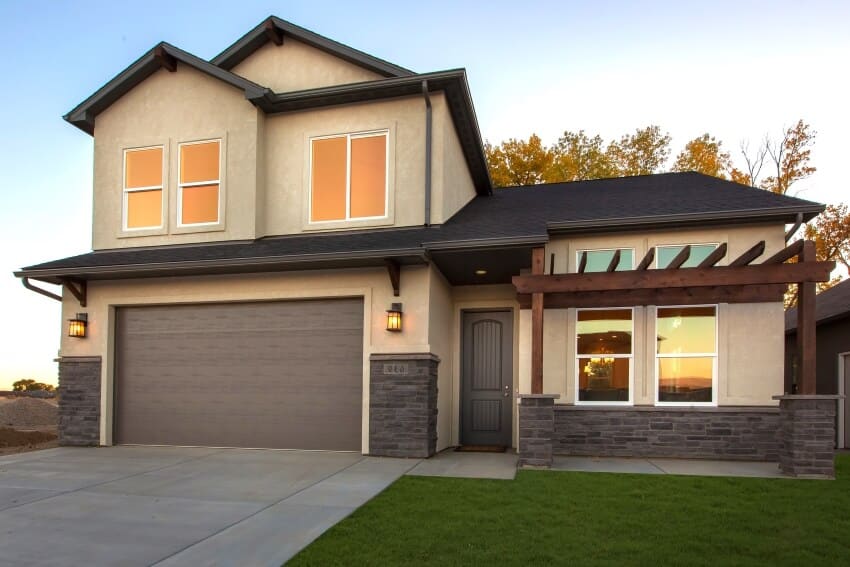 Modern two story house with wood pergola, garage, and cream colored siding with stone base