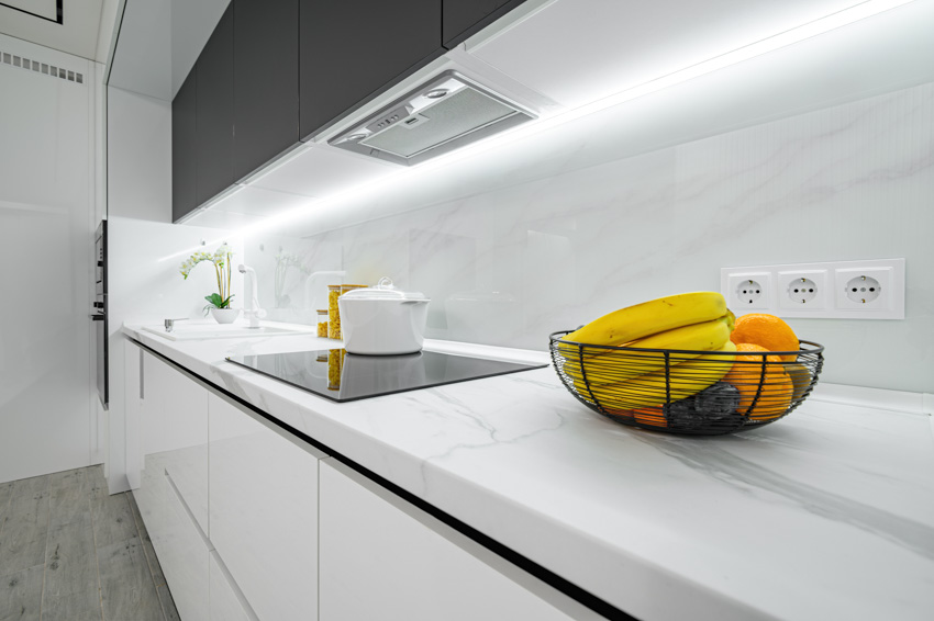 Modern white kitchen with quartz countertop that looks like Carrara marble backsplash, range hood, stove, and cabinets