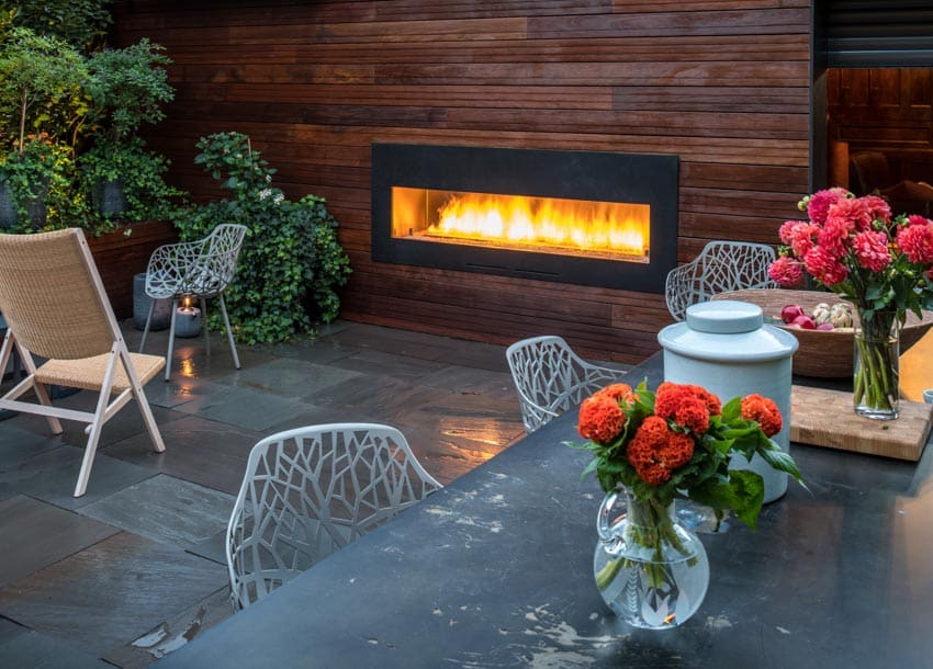 Outdoor patio with electric fireplace, beaded fireplace wall made of wood, stone tile flooring, chairs, and table