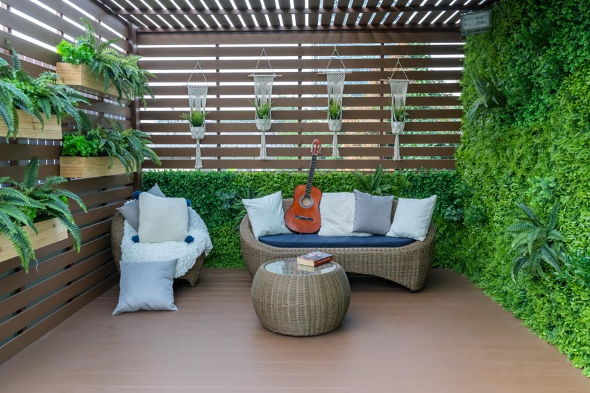 Outdoor patio with couch, accent chair, privacy fence, hanging plants, and outdoor ottoman
