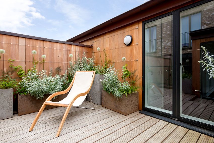 Simple attractive modern urban balcony garden with okoume wood accent walls, potted plants and a reclining chair