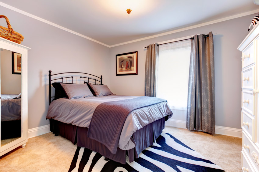 Simple bedroom with pillows, bedding, mirror, window, curtains, and lavender painted wall