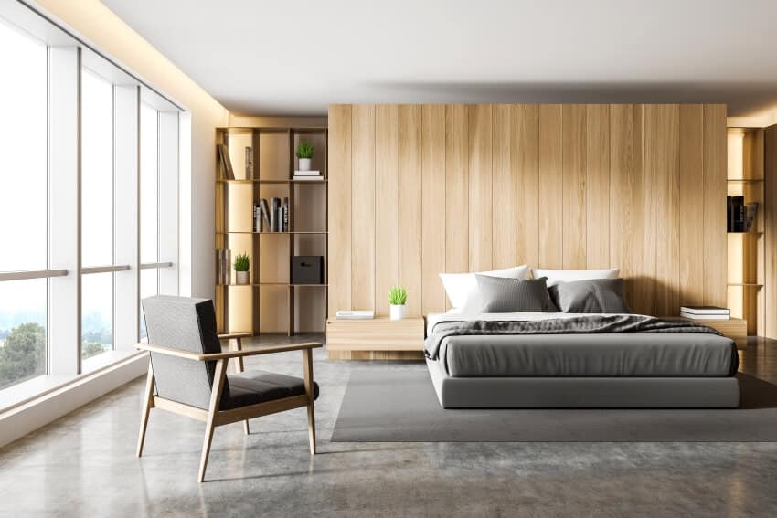Sleek modern bedroom with wooden walls, concrete floor, bookshelves, and gray armchair