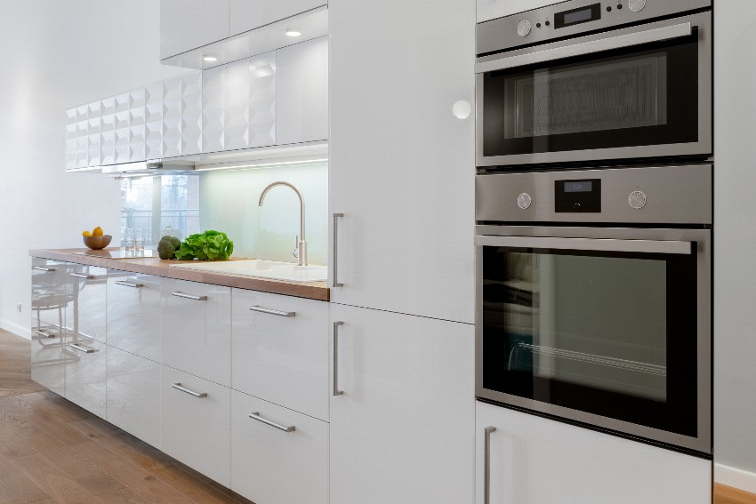 Small kitchen with white pvc cupboards and drawers, wooden floor and stainless steel oven and microwave