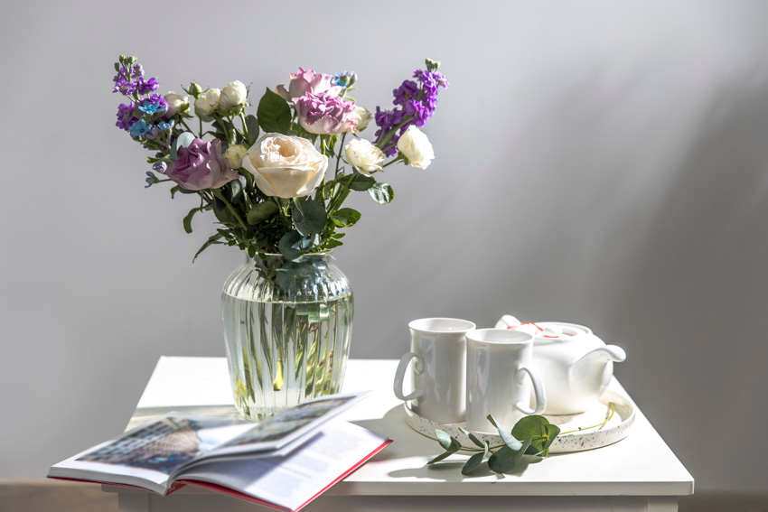 Small table with glass vase, flowers, and tea set for home interiors
