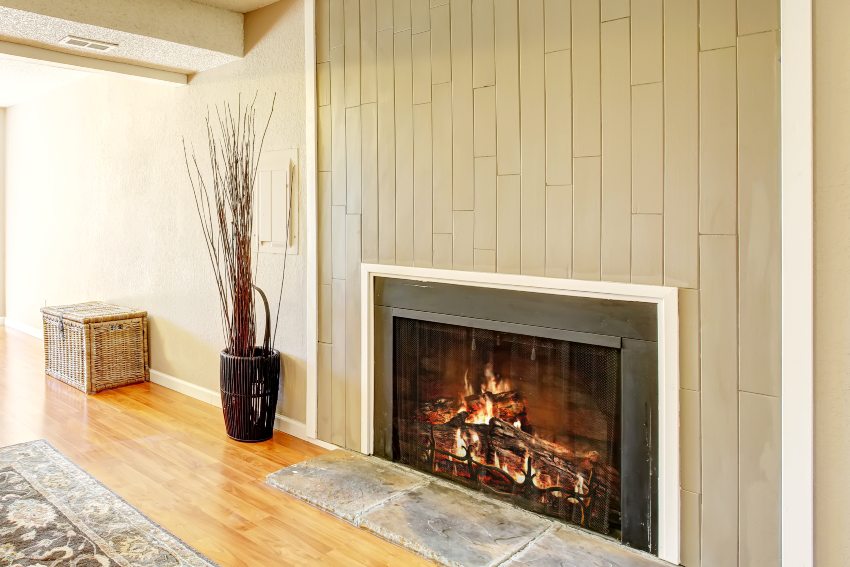 Spacious empty living room with vertical shiplap on fireplace decorated with wicker chest and dry bushes