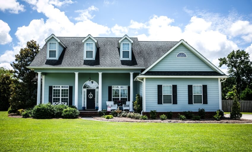 Teal house with large front yard, black roof, columns, and traditional windows and shutters