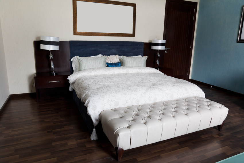 Traditional bedroom with rectangle ottoman, bedding, nightstands, headboard, lamps, and wood floor