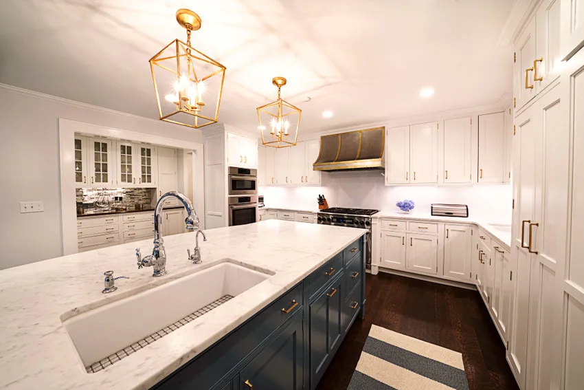 Traditional kitchen with island, pendant lights, sink, faucet, Carrara marble countertop, white cabinets, backsplash, wood flooring, and range hood