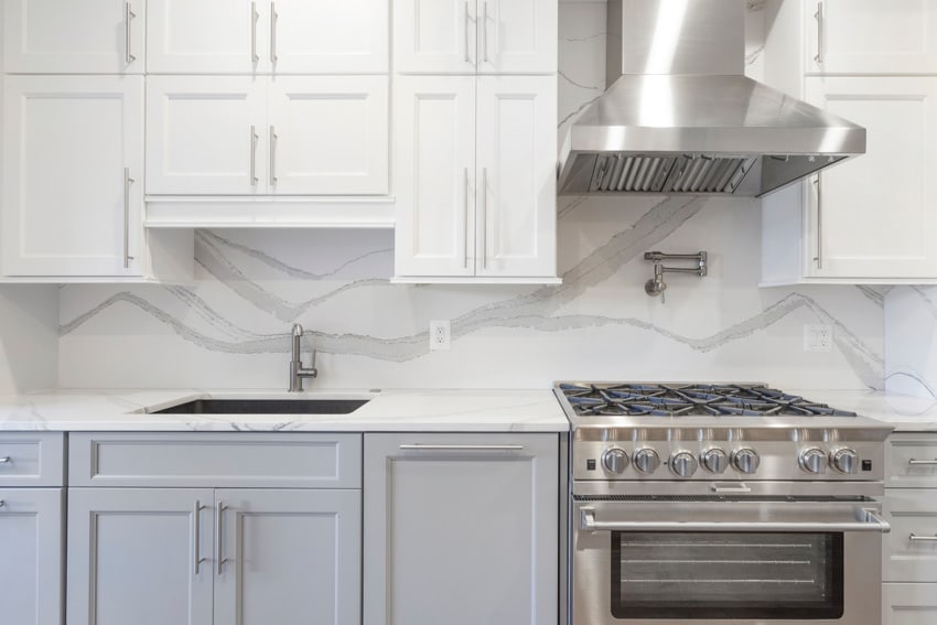 Traditional kitchen with marble slab backsplash, cabinets, range hood, stove, oven, sink, and faucet