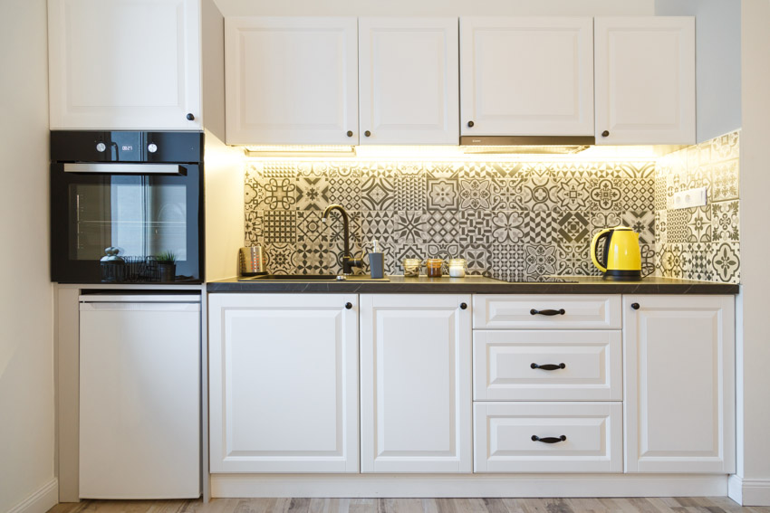 Traditional kitchen with white cabinets, Spanish tile mosaic backsplash, countertop, oven, and drawers