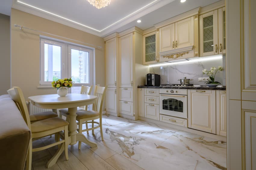 Traditional kitchen with white cabinets, oven, LED lights under the cabinet, table, chairs, window, and marble slab backsplash