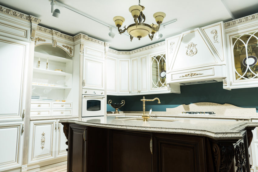 Victorian kitchen with brass faucet, island, contertops, white cabinets, range hood, and chandelier