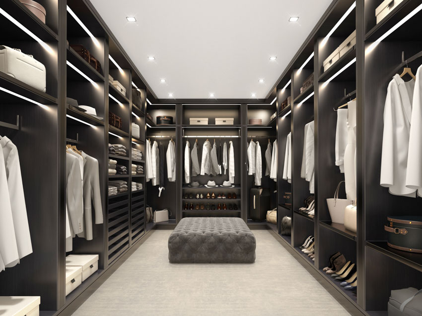 Large walk-in closet with tufted bench and black cabinets
