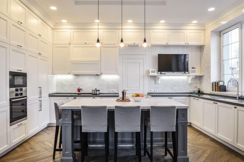 Contemporary kitchen with white cabinets, oven, windows, island, chairs, pendant lights, sink, faucet, and Carrara marble tile backsplash