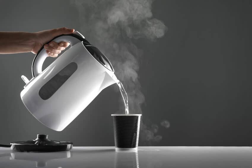 White electric kettle pouring water in black cup on kitchen countertop