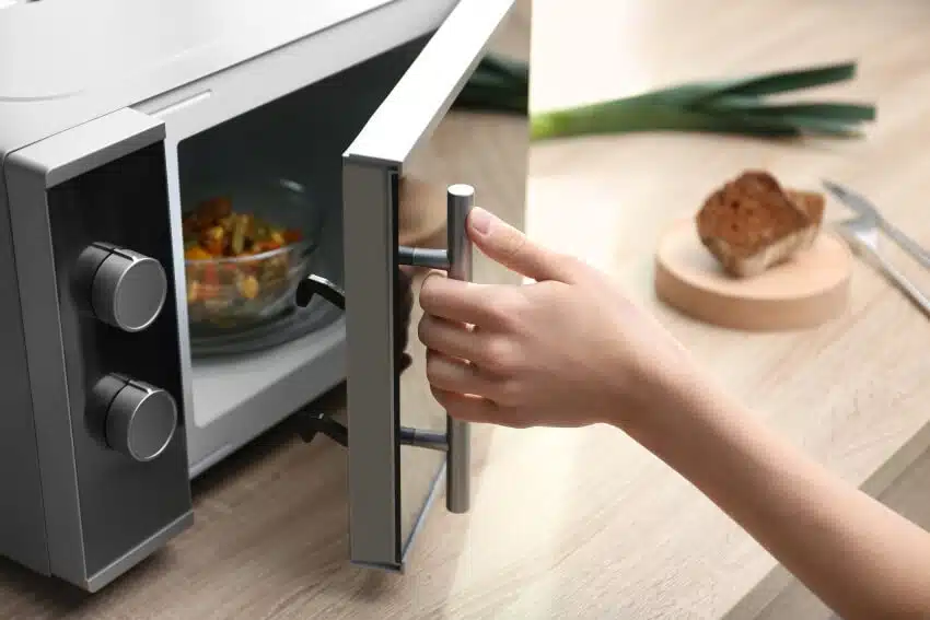 Woman using microwave oven on wooden countertop in kitchen