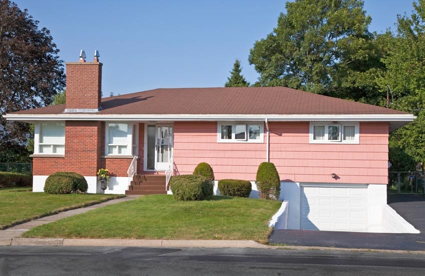 1960s traditional suburban house with pink siding, low pitched roof, chimney, windows, front door, garage, and lawn