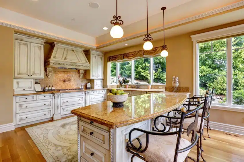 French country kitchen with backsplash, countertops, island, cabinets, range hood, chairs, rug, wood flooring, pendant lights, and windows