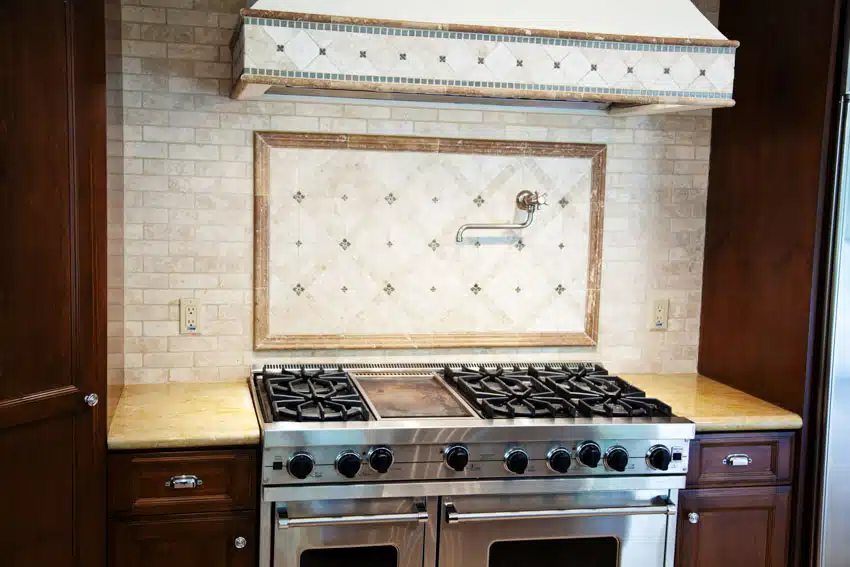 French country kitchen with with white brick backsplash, range hood, and stove