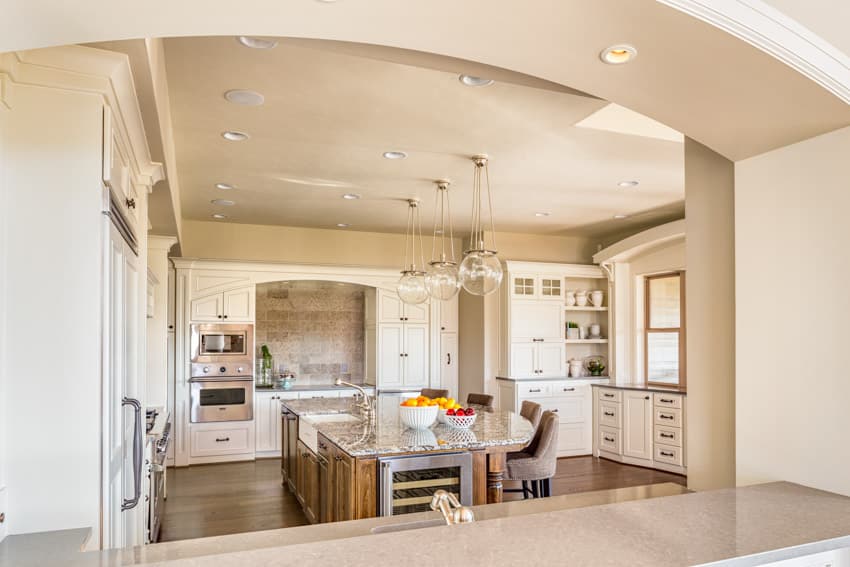 Kitchen with island, chairs, wine cooler, arched doorways and glass hanging lights