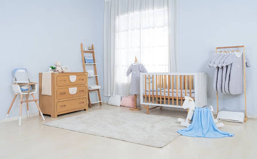 Nursery room with wooden crib high chair drawer rug light blue paint
