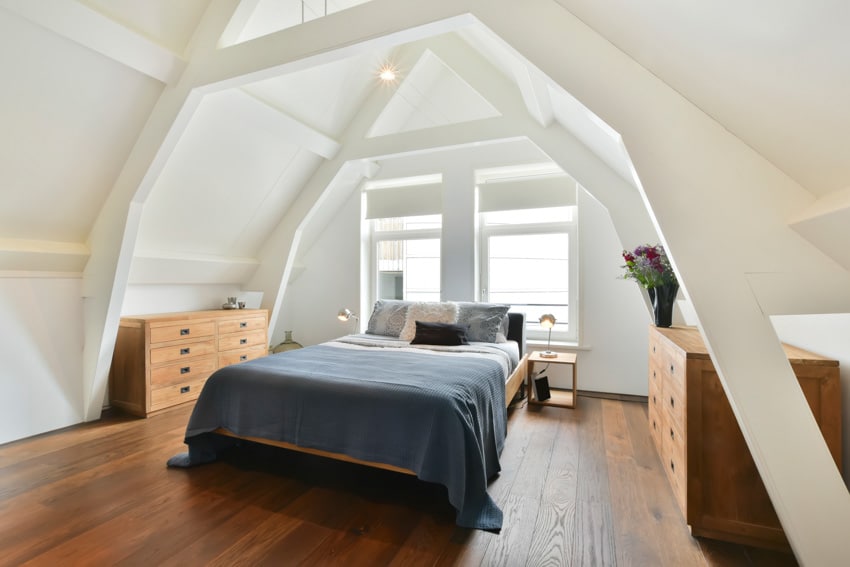Attic bedroom with two dressers, comforter, wood floors, angled ceiling, windows, and pillows