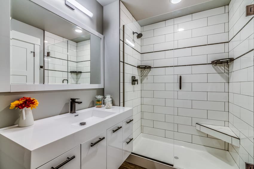 Bathroom shower with white subway tile and black grout, vanity area, mirror, sink, cabinets, and ceiling lights