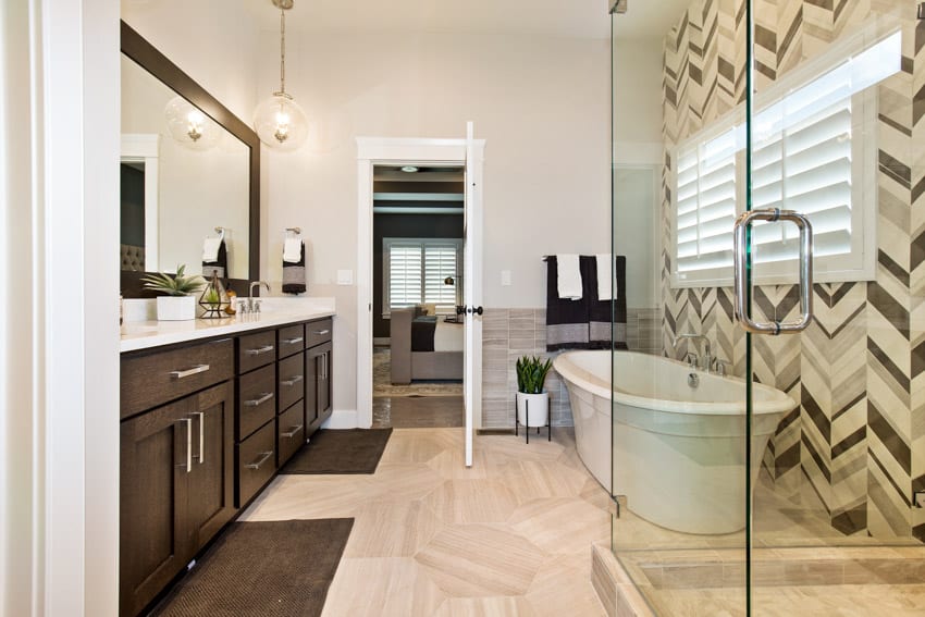 Bathroom with chevron tile backsplash, tub, glass shower enclosure, windows, wood cabinets, countertop, and vanity mirror
