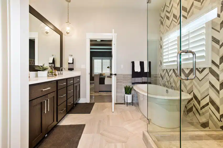 Bathroom with glass accent wall tile, tub, glass shower enclosure, windows, wood cabinets, countertop, and vanity mirror