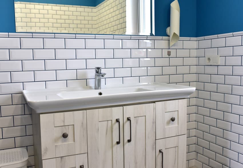 Bathroom with countertop, sink, cabinet, white subway tile and black grout backsplash, and mirror