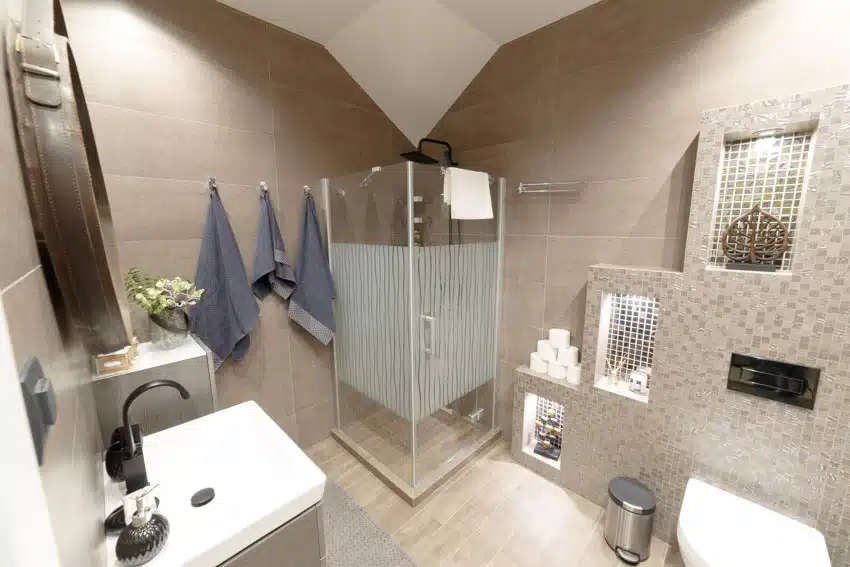Bathroom with glass shower enclosure, matte porcelain tile wall, sink, faucet, toilet, and towel holder
