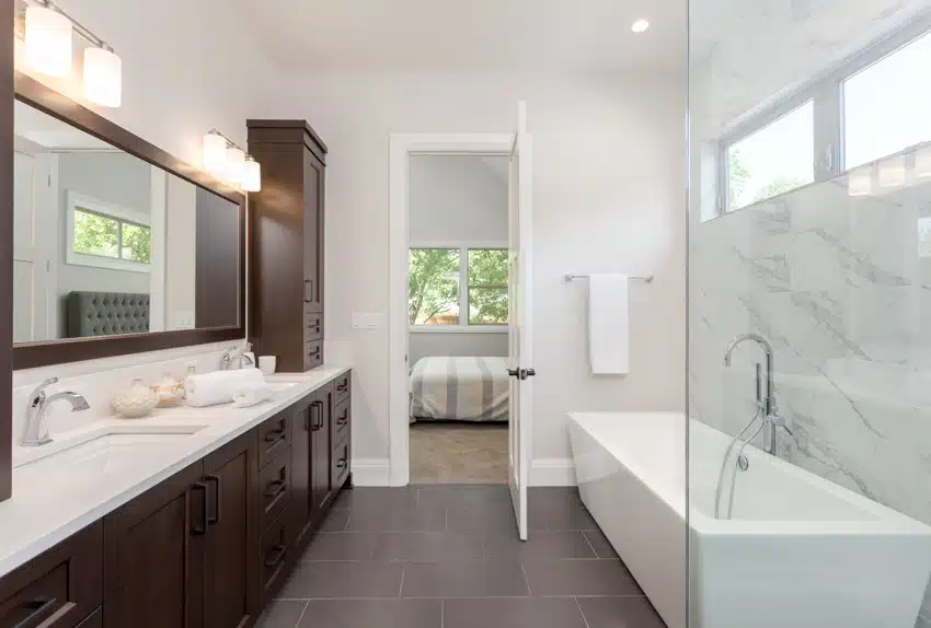 Bathroom with matte porcelain tile floor, tub, window, countertop, cabinets, wall sconces, and windows