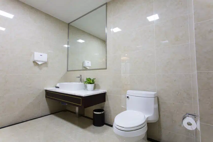 Bathroom with polished porcelain tile wall, mirror, toilet, countertop, sink, and faucet