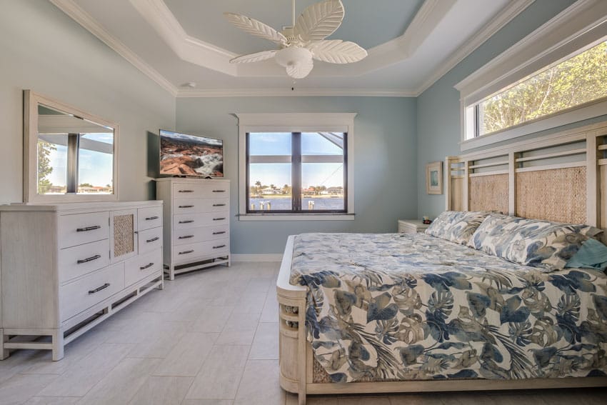 Beach house bedroom with two dressers, ceiling fan, mirror, headboard, and windows