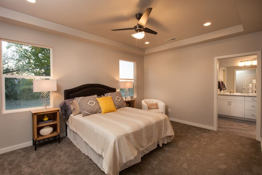 Bedroom with ceiling fan controlled by a light dimmer, pillows, nightstand, lamp, and windows