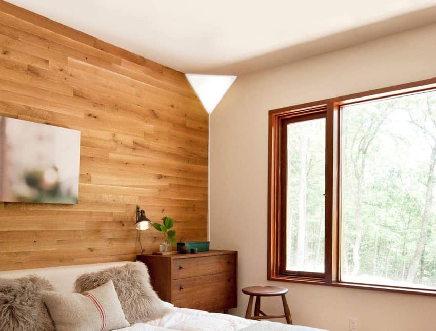 Bedroom with corner wall sconce, wood accent wall, stool, dresser, and window