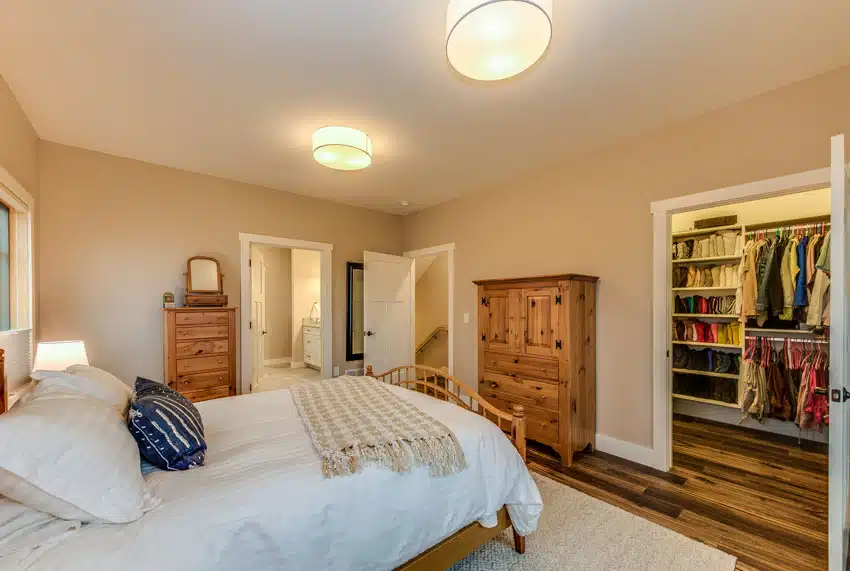 Bedroom with two tall dressers, walk-in closet, wood flooring, comforter, pillows, and ceiling lights