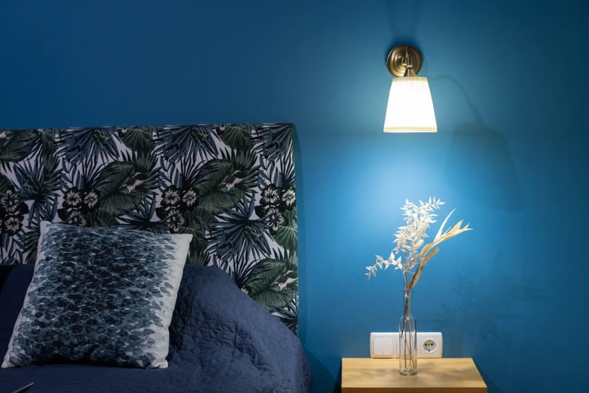 Bedroom with wall sconce, nightstand, pillow, headboard, and blue painted wall